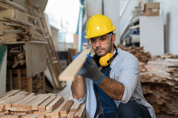 Male carpenter working in wood workshop. Male joiner wearing safety uniform, gloves, helmet and...