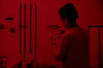 Rear view of young photographer working with photo film in darkroom
