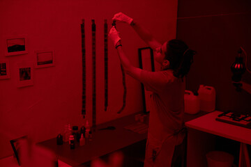 Rear view of young photographer hanging photo film on the rope working in darkroom