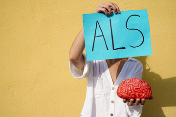 unrecognizable woman holding a als acronym card and a brain. Muscle and neurone illness. Amyotrophic Lateral Sclerosis day