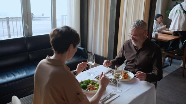 Blonde waitress brings food for happy elderly couple in cafe