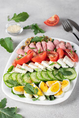 Healthy cobb salad with ham, feta cheese, cucumber, tomato, olives and eggs on white plate. Ketogenic lunch