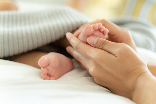 Mom and Newborn,Happy family concept.Close up view of beautiful Asian mother and her sleeping newborn baby.Mother holding baby hand in one hand and holding hand the baby with eyes closing and smiling.