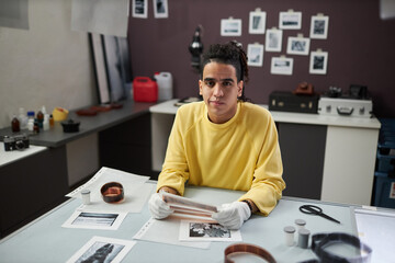 Portrait of young photographer looking at camera while sitting at his workplace and working with...