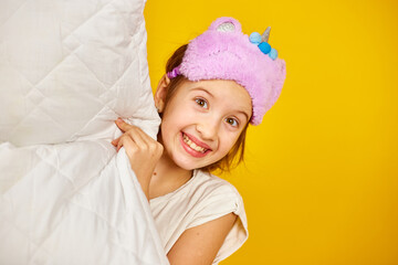 Funny teenage girl in white pyjamas with a violet sleeping mask hold pillow