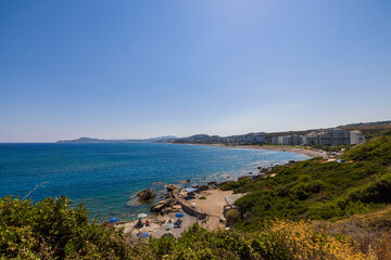 Fototapeta na wymiar Beautiful view of people on rocky coastline beach on sunny summer day on background hotels. Greece. Rhodes.