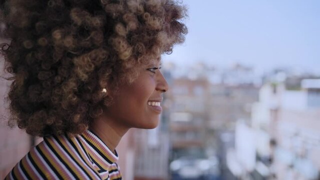 Happy young black woman with afro hair smiling. Cheerful African American girl watching outdoors in open air. Portrait of female with positive expression looking out of window. Copy space.