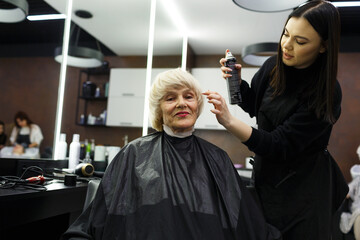 Portrait of an elderly woman visiting a professional hairdresser. An experienced hairdresser does hair styling for a client.