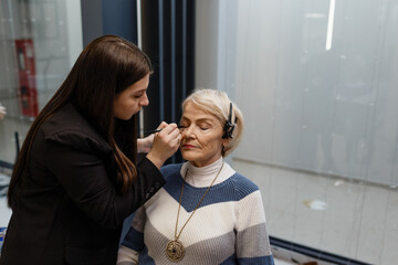 An elderly woman visiting a professional makeup artist. An experienced makeup artist does makeup for a client