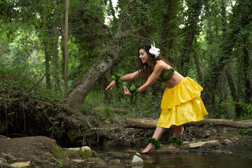 A happy and young woman is performing hula dance in nature on the river bank.