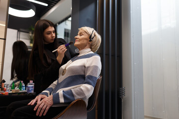 Fototapeta na wymiar An elderly woman visiting a professional makeup artist. An experienced makeup artist does makeup for a client