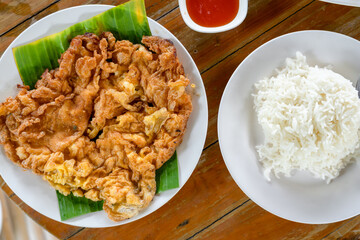Omelet fried eggs and chili sauce in Thai style served on banana leaf in white plate with cooked rice on wooden table in restaurant. Thai Asian cuisine food.