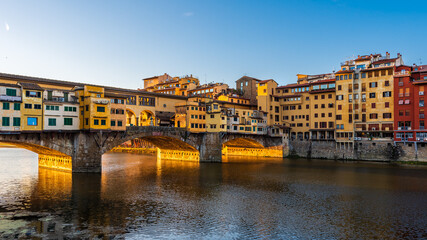 UNESCO site bridge Ponte Vecchio with golden arches in Florence early in the morning sunlight.
