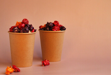 Multicolored popcorn in caramel glaze in a paper cup on a pink background