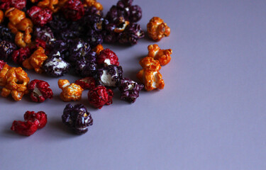 Multi-colored popcorn in caramel glaze scattered on a lilac background