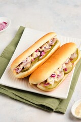 Dutch style sandwiches with pickled cucumber, herring, onion and mustard sauce in a bun on a white plate on a light concrete background.