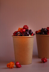 Multicolored popcorn in caramel glaze in a paper cup on a pink background
