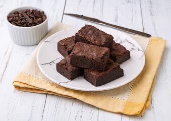 Brownies on a plate with chocolate pieces over white wooden table
