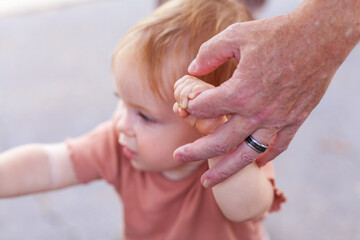 Grandfathers hand holding baby's hand helping baby to walk