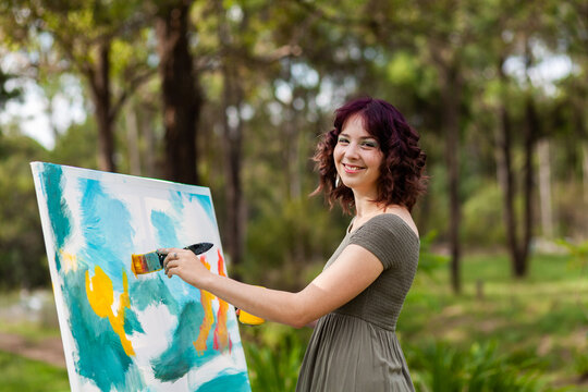 Young creative artist with curly purple hair working on canvas with acrylic paints