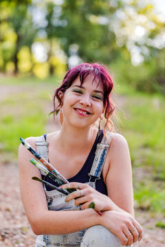 Smiling portrait of young woman artist painter holding art brushes