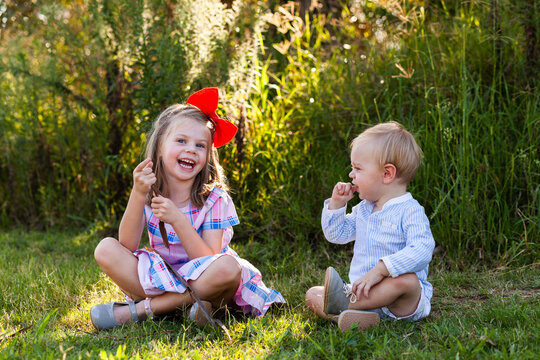 Happy brother and sister sitting together on grass at park outside in nature