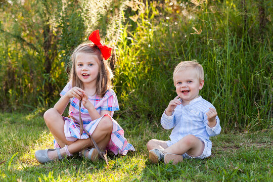 Happy brother and sister sitting together on grass at park outside in nature