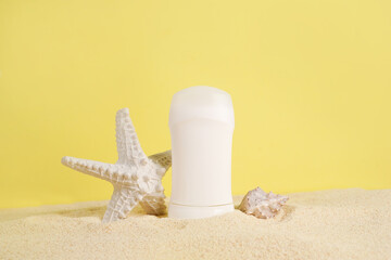 White antiperspirant, deodorant and sea star on the sand on yellow background. Concept of sea mineral toiletries and organic summer cosmetics. Body care. Copy space