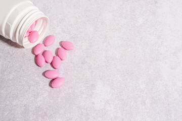 Pink pills pouring out of the white bottle on light concrete background, medicine