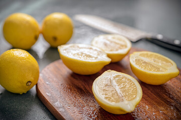 Sicilian lemons cut on wooden board and other lemons arranged next to it with a knife in the background.