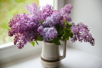 Bouquet of blooming lilac in a vase on the windowsill by the window