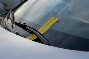 Close up of a yellow parking ticket placed at the car front on the windshield under wiper blade.