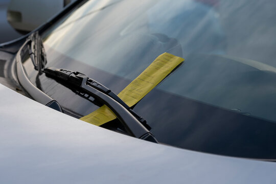 Close up of a yellow parking ticket placed at the car front on the windshield under wiper blade.