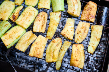 Close-up top view of zucchini slices, being marinated and cooked over flaming charcoal barbecue grill in the backyard. BBQ party. The concept of preparing food in the open air and summer chill out