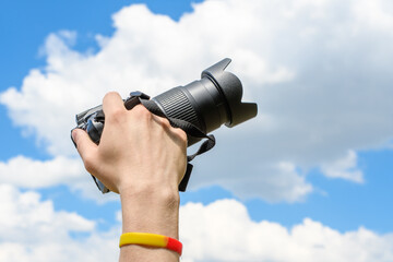 Dłoń trzymająca aparat fotograficzny na niebieskim tle chmur na niebie  - obrazy, fototapety, plakaty
