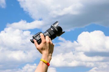 Dłoń trzymająca aparat fotograficzny na niebieskim tle nieba. Chmury wychodzące z aparatu