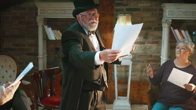 Elderly acter recites his lines  while other actors listen rehearsing  scene