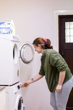 young woman in laundry turning on washing machine