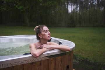 Beautiful happy woman enjoys hot tub SPA outside surrounded by forest scenery