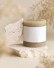 Candle with label on beige stone near dried pampas grass close up, copy space, mock up
