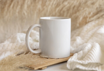 White coffee mug on wooden tray near pampas grass and cosy sweater, Close up, mock up