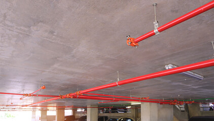 Selective focus at sprinkler with red fire protection water pipeline system on concrete ceiling inside of parking garage building - obrazy, fototapety, plakaty