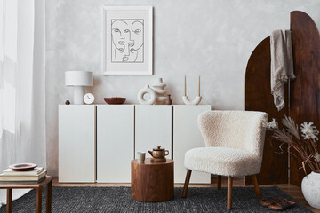 Creative composition of cozy living room interior design with mock up poster frame, fluffy armchair, folding screen, coffee table, commode and personal accessories. Modern style. Template.