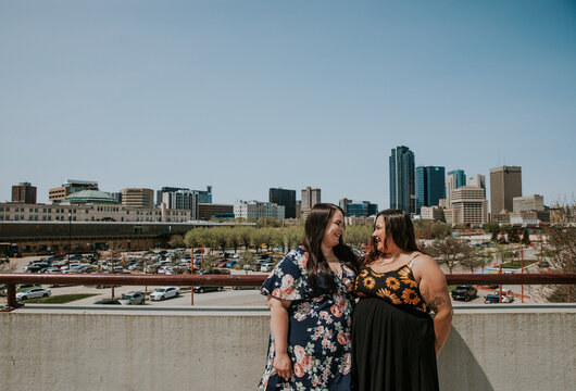 2 women stand on a rooftop overlooking the city