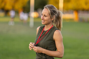female sports coach with pony tail holding whistle on red tape around her neck