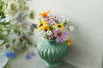 Stylish colorful wildflowers bouquet on tile shelf on rustic wall background. Beautiful summer flowers in vase gathered from garden, floral arrangement in modern room in home