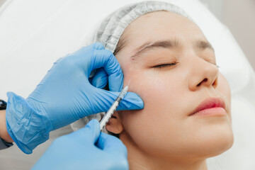 Close-up of the hands of a beautician injecting Botox into a woman's forehead. Correction of forehead and eye wrinkles with botulinum toxin.