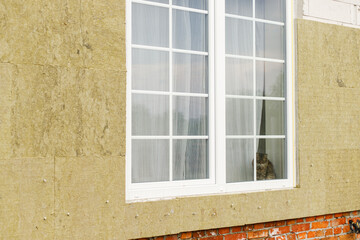 Facade insulation with mineral wool, thermal improvement and energy saving. Modern farmhouse renovation covering with stone wool panels and cute cat in window. House insulation concept