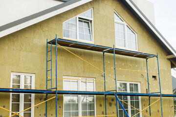 Facade insulation with mineral wool, thermal improvement and energy saving. Modern farmhouse renovation, scaffolding platform and stone wool panels. House insulation concept