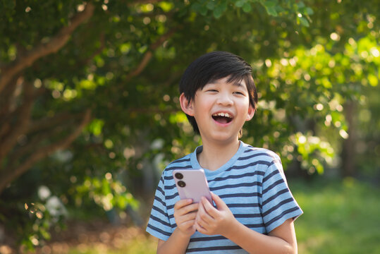 Happy Asian child playing game on mobile phone in the park outdoor
